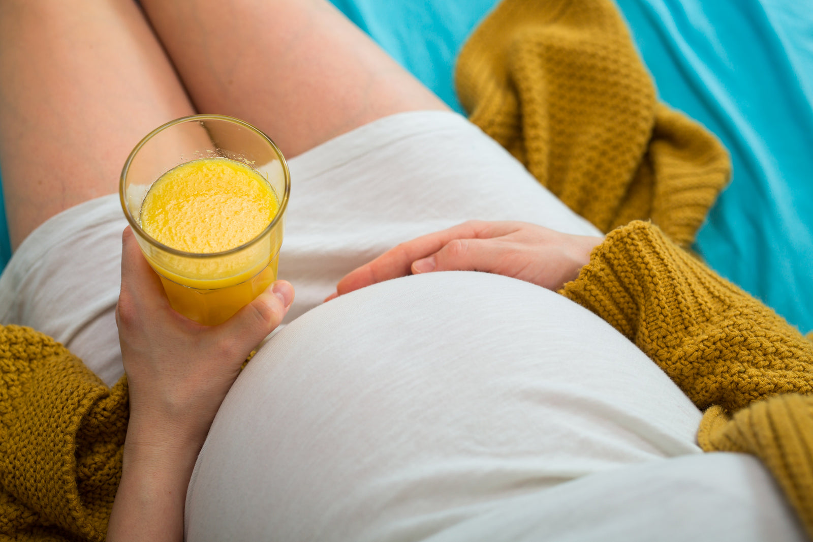 Pregnant woman with heartburn sitting down holding her bump and a glass of orange juice