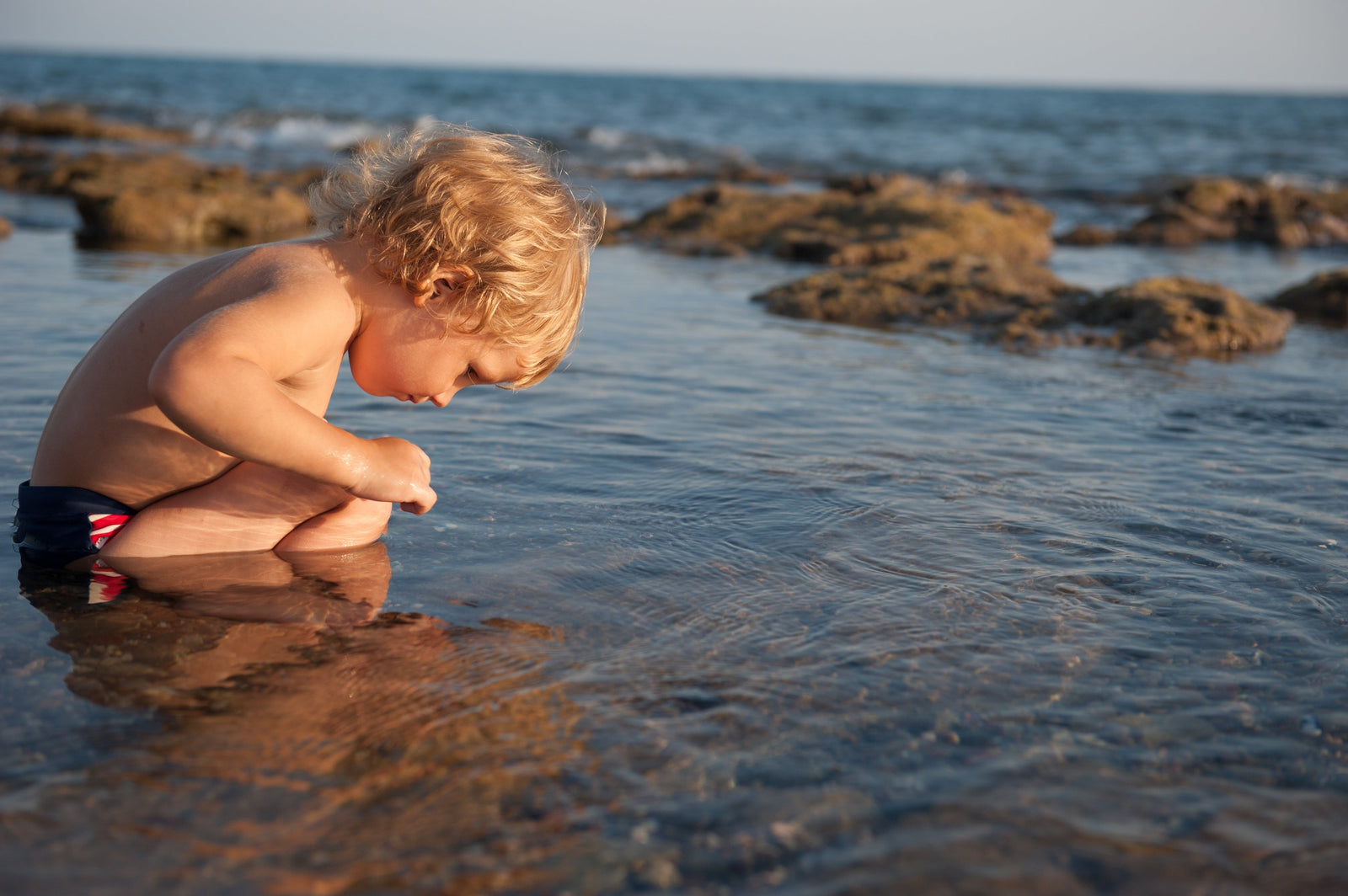 Young boy with blonde hair crouching in a rock pool