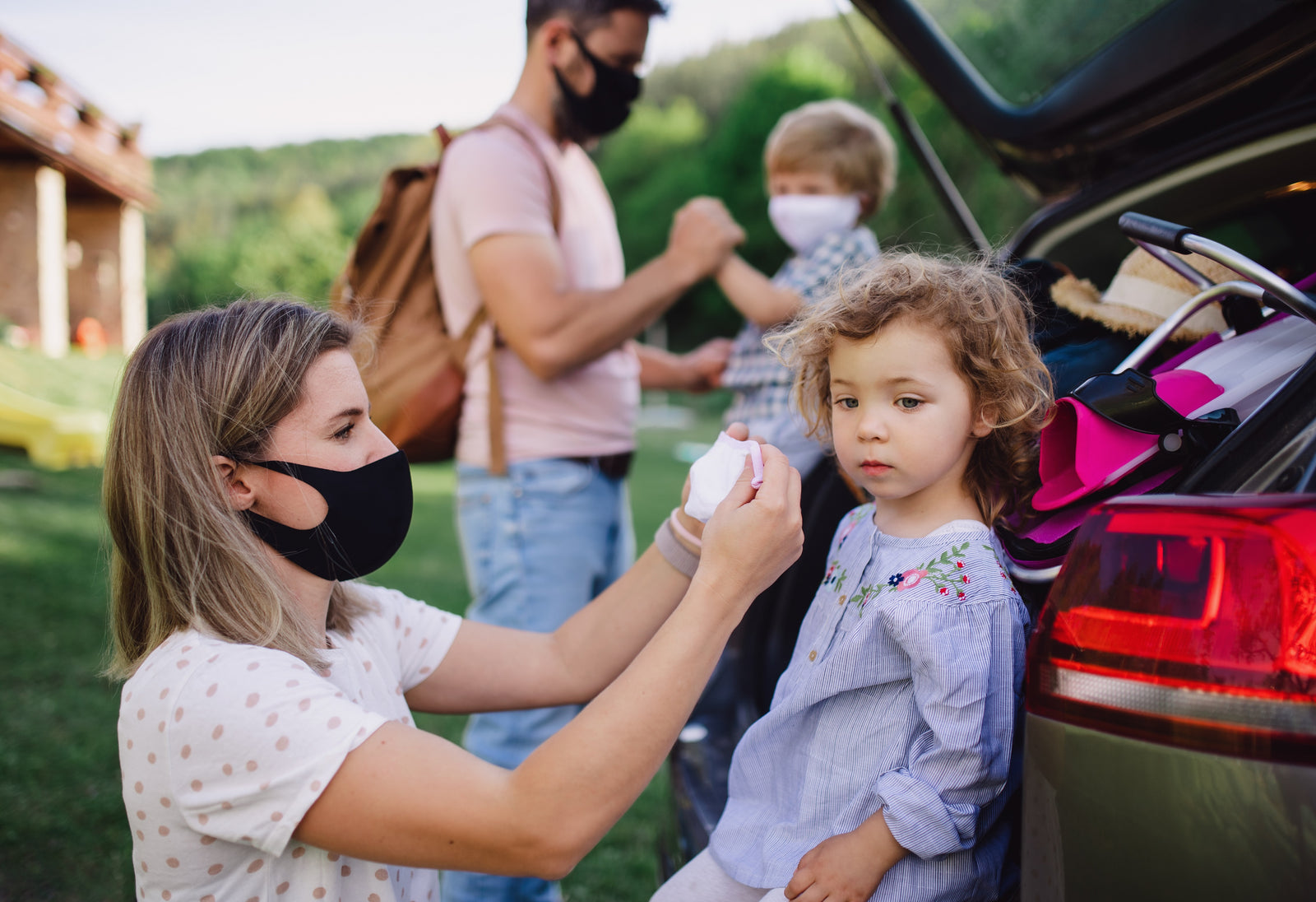 Family wearing and putting on masks by a car