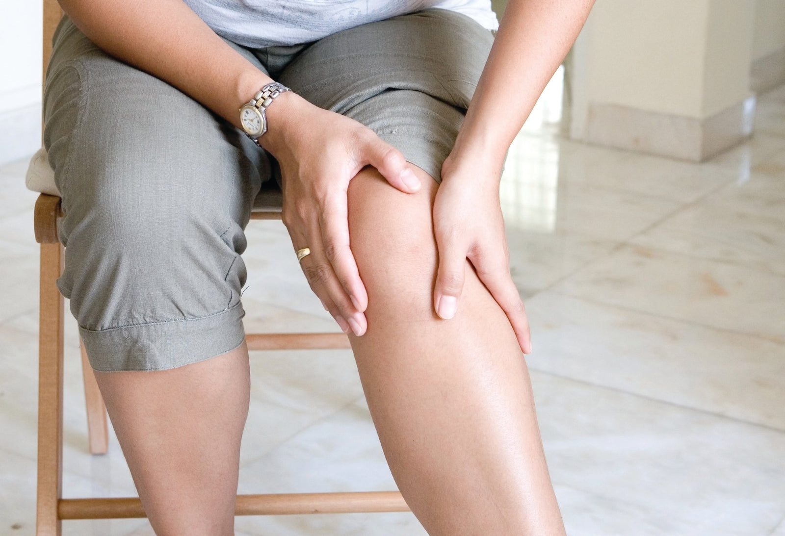 Lower body of woman sat on chair with both hands holding her knee which is in pain