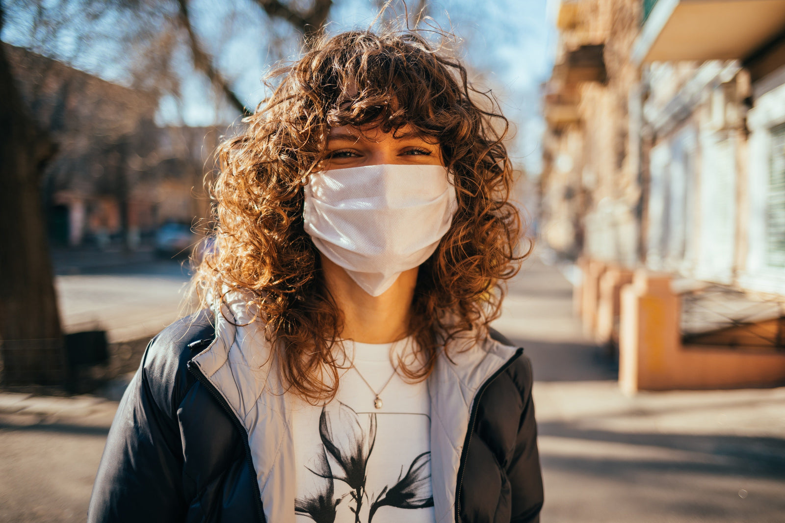 Woman with curly hair wearing white face mask outside