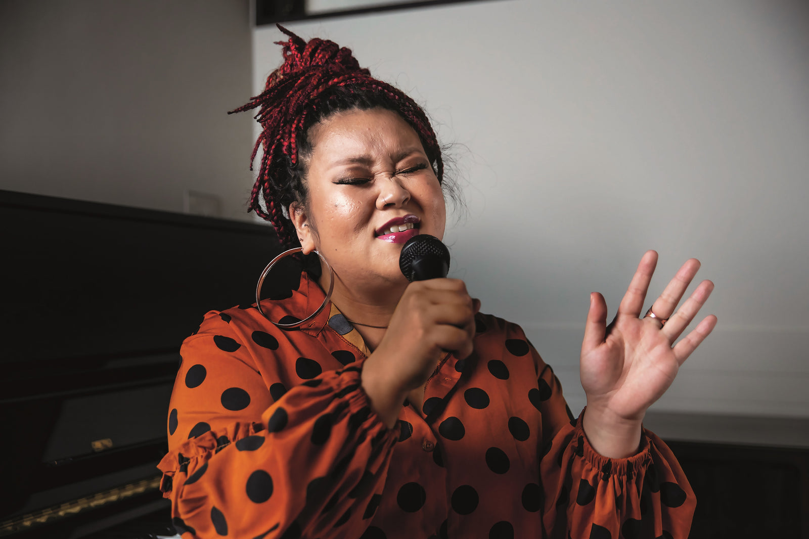 Woman in a red and black spot top singing into a microphone