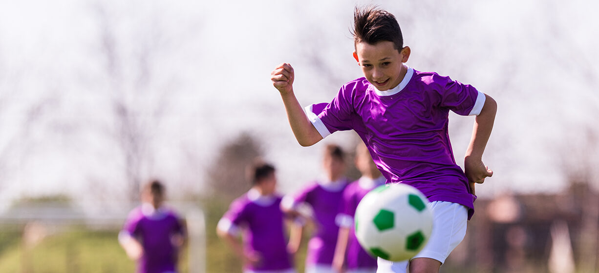 Young boy  with short dark hair and purple sports top playing football