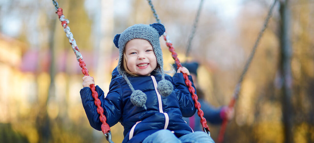 Little girl dressed in winter outdoor clothes and playing on a swing