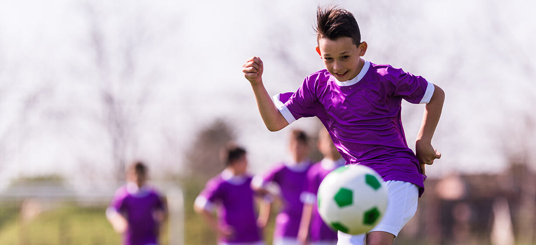 Young boy  with short dark hair and purple sports top playing football 